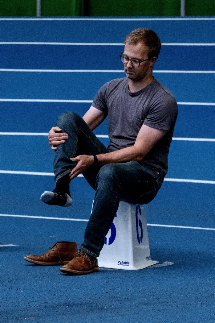 Man sat on a numbered cone taking off shoe - blue