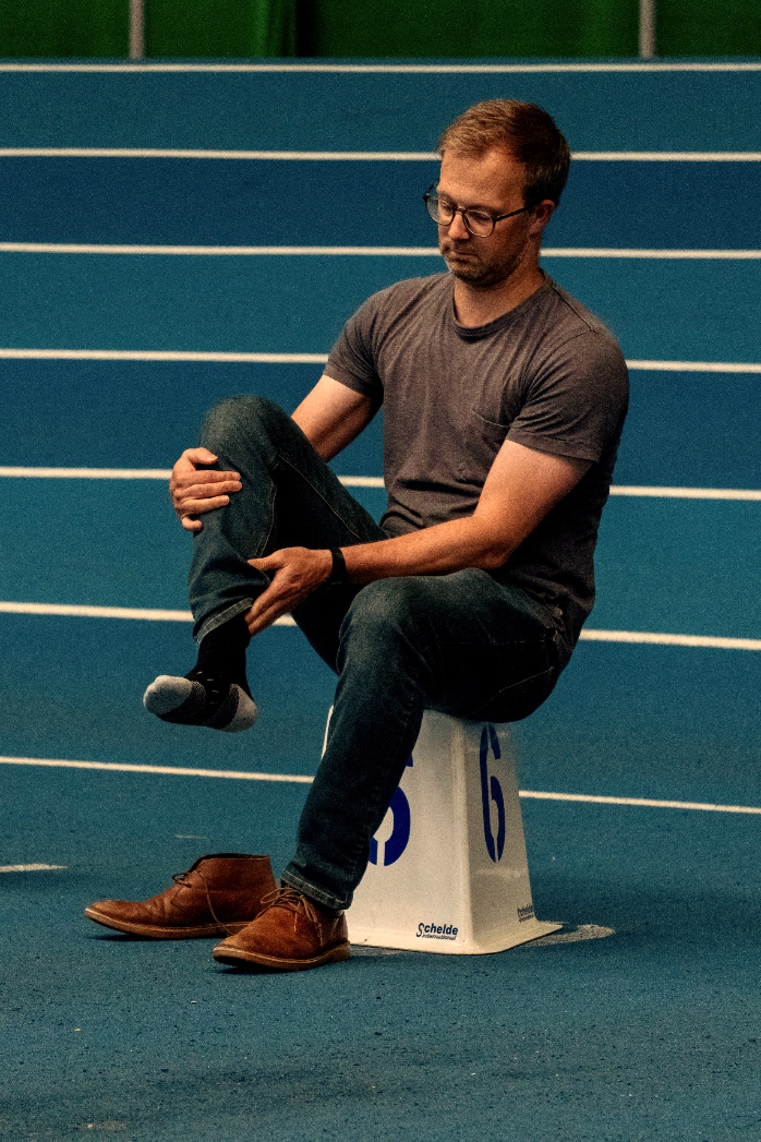 Man sat on a numbered cone taking off shoe - yellow